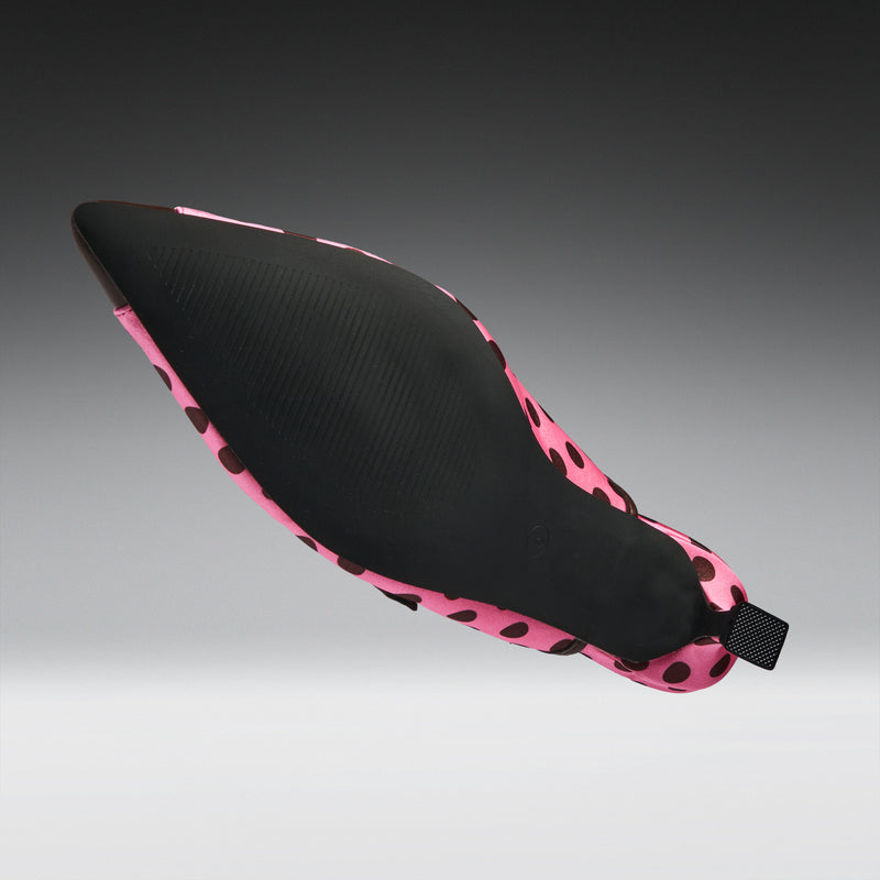 A single pointed-toe shoe shown floating against a dark-to-light gray gradient background. The upper is black with a pink and black spotted pattern around the edges and heel.
