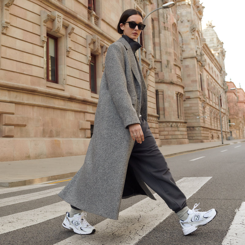 Women’s wide white and navy sneakers on feet with white laces and dark outerwear.