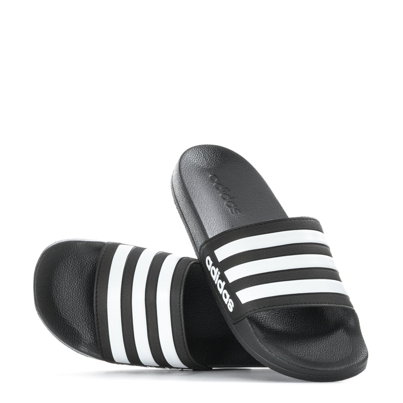 Black youth slide sandals with white three stripes; one sandal shows curved footbed
