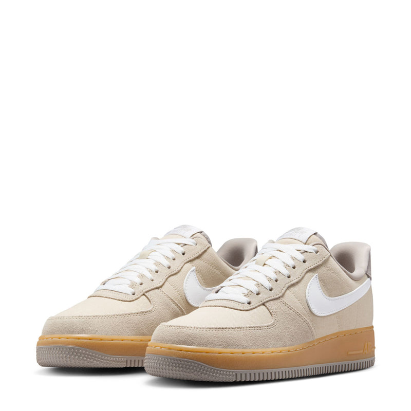 Pair of Nike Air Force 1 low-top sneakers, light khaki with white swoosh and gum soles.