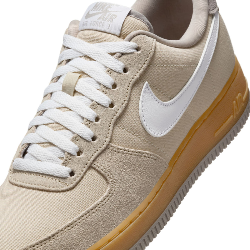 Nike Air Force 1 upper close-up: light khaki suede, white laces, white swoosh, gum trim.