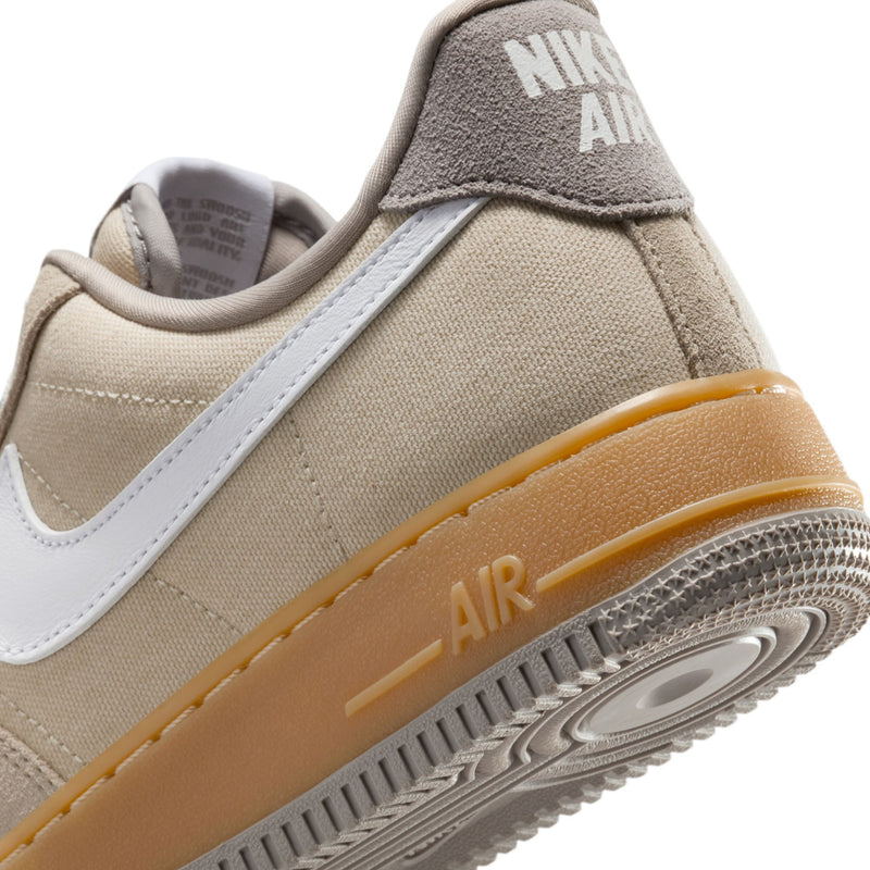 Nike Air Force 1 close-up: light khaki heel, white swoosh, gum midsole with AIR text.