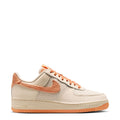 Women’s Air Force 1 low-top sneakers in cream with orange swoosh, laces, and gum sole.