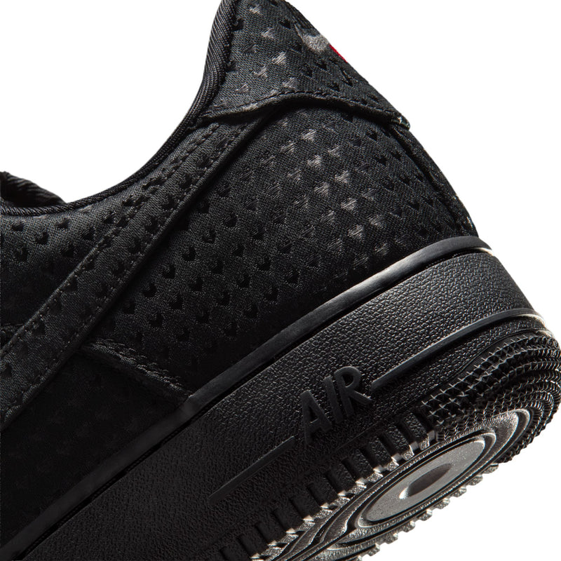Close-up of black sneaker side panel with stitched swoosh and black rubber sole edge