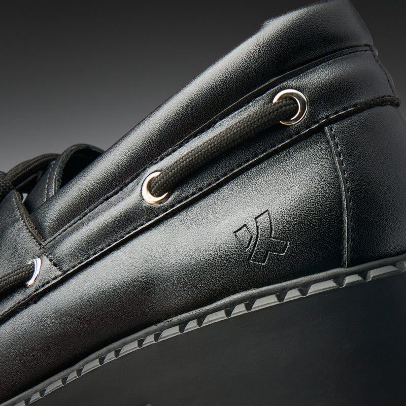 Close-up of a black leather shoe with a brand logo on a dark background