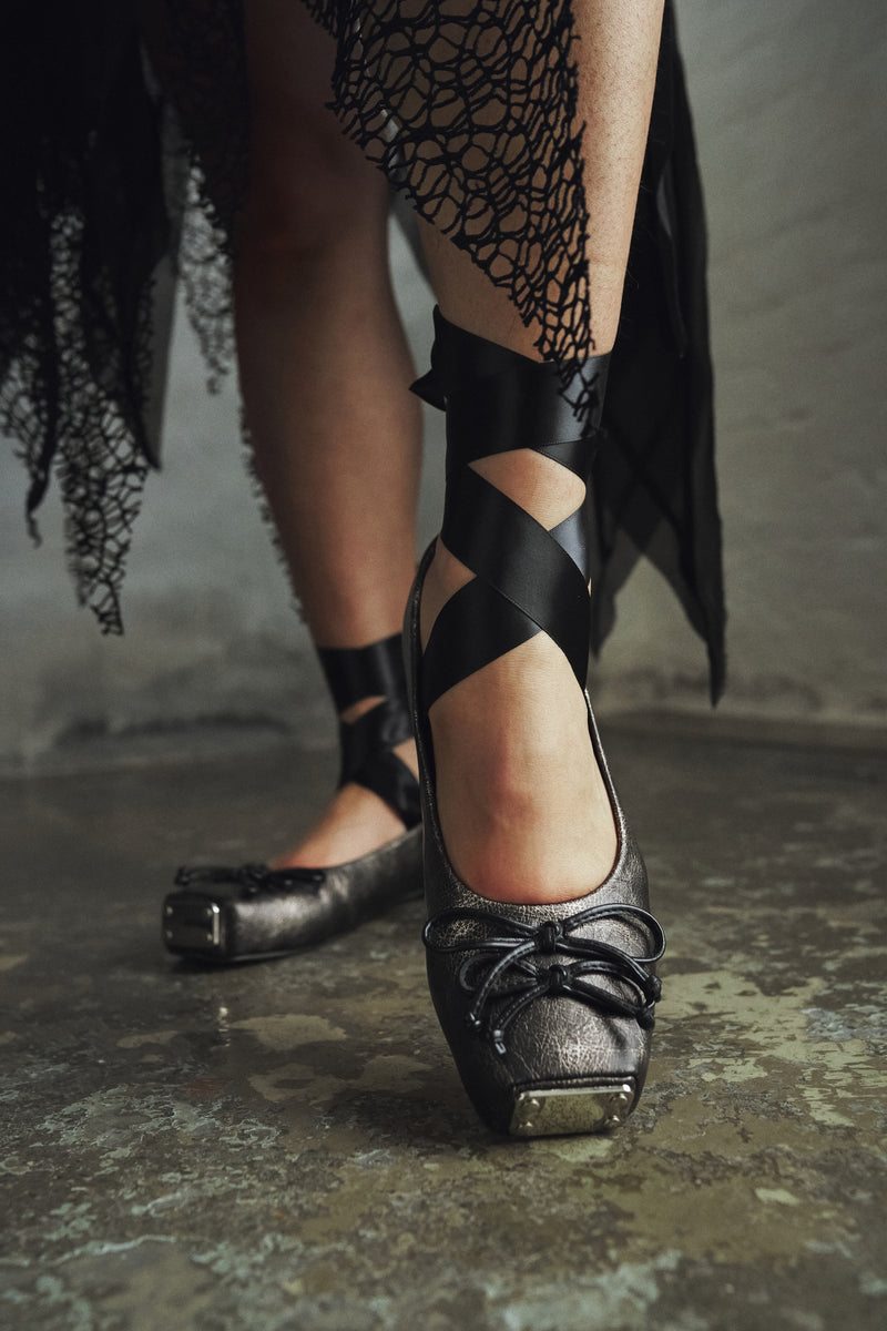 Black high-heeled shoes with criss-cross straps worn by a person on a textured floor.