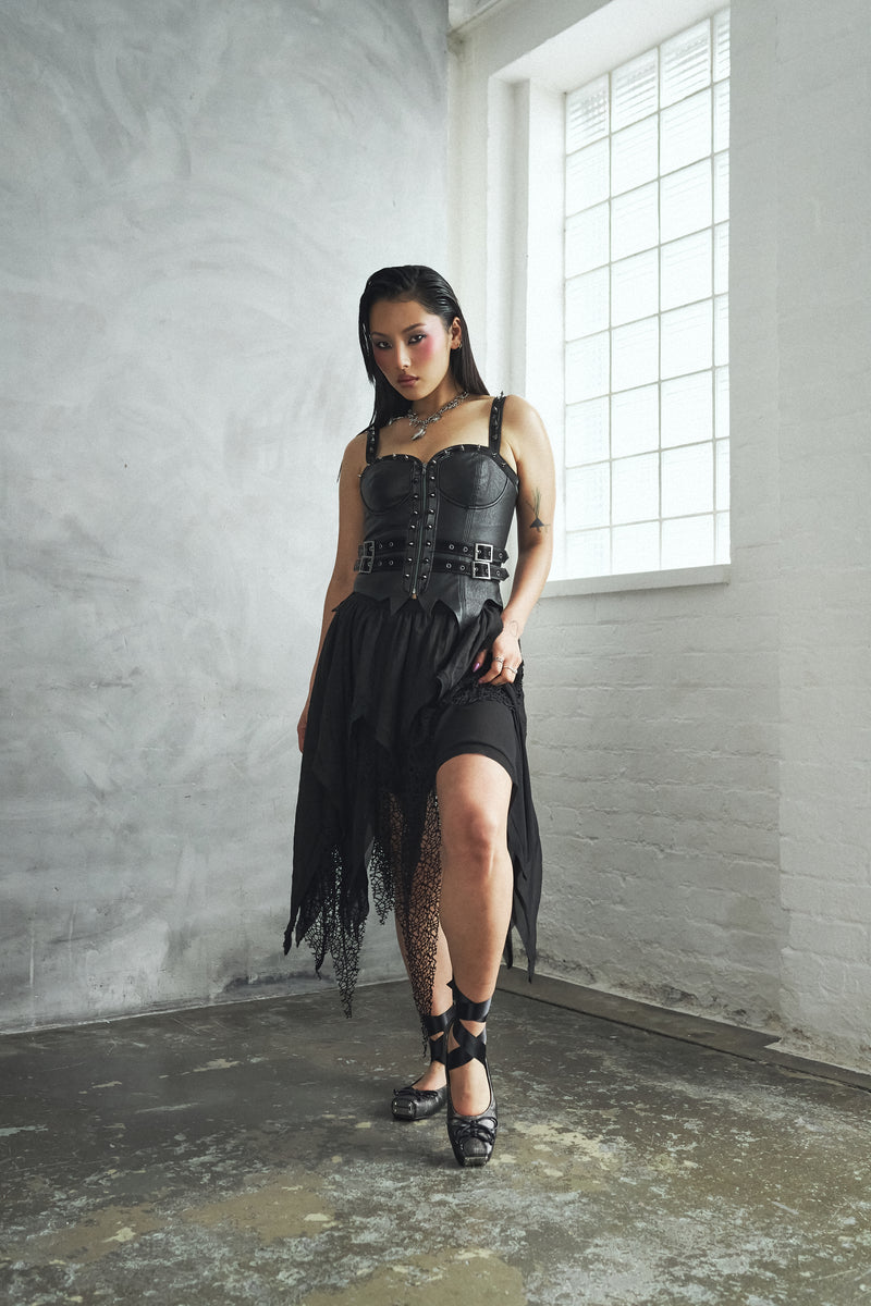 Woman wearing a black dress with fringe in a room with concrete walls and a window.