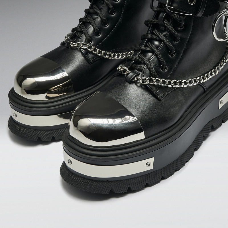 Black platform boots with metallic tops and chains on a light gray background