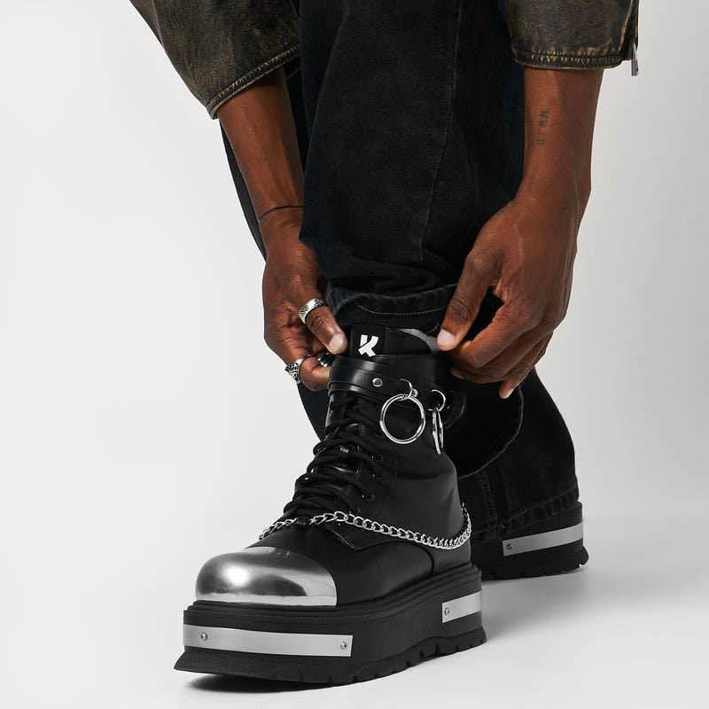Model wearing black high-top boots with chain details on a gradient background