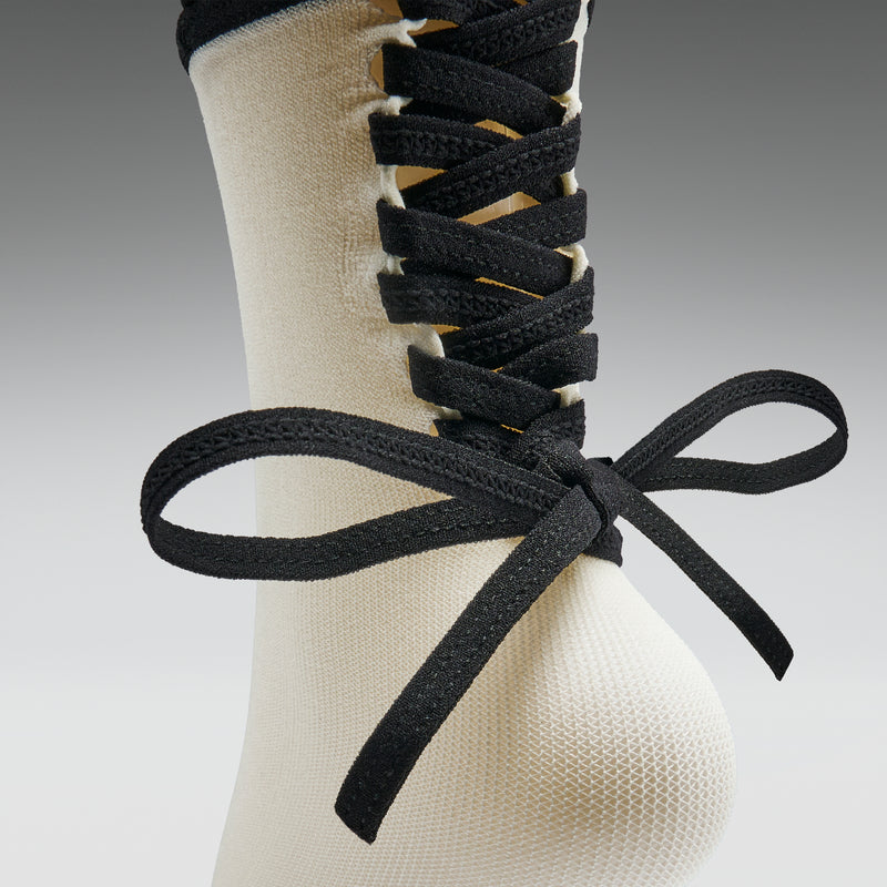 Close-up of a foot wearing a white sock with black lace-up shoes on a gray background