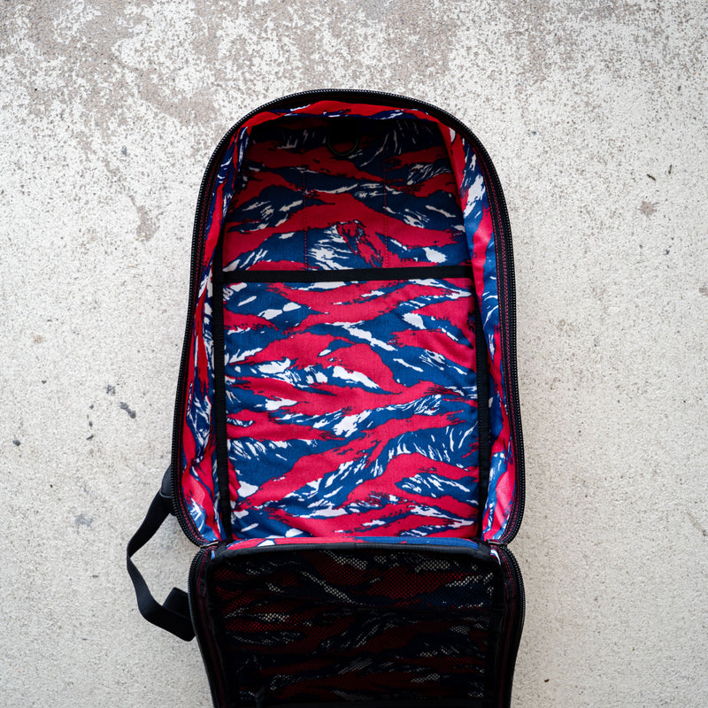 The Bullet Ruck Classic - Ballistic Nylon Cordura is open, revealing its red, blue, and white patterned lining as it lies on a concrete surface.