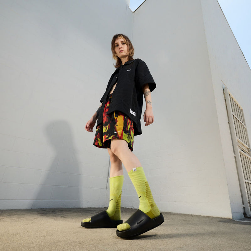 Womens black slide sandal worn with neon socks and a patterned outfit