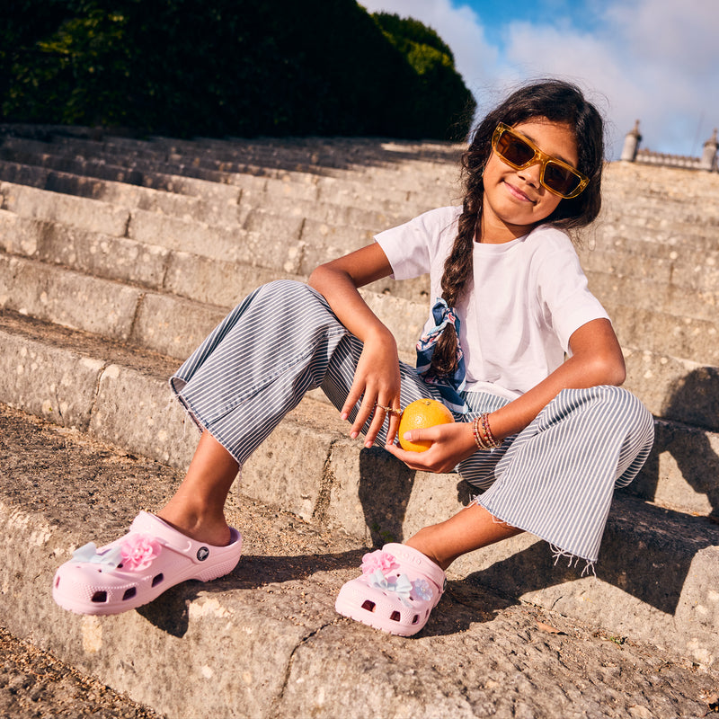 Pair of light pink youth clogs with floral and bow-like accents