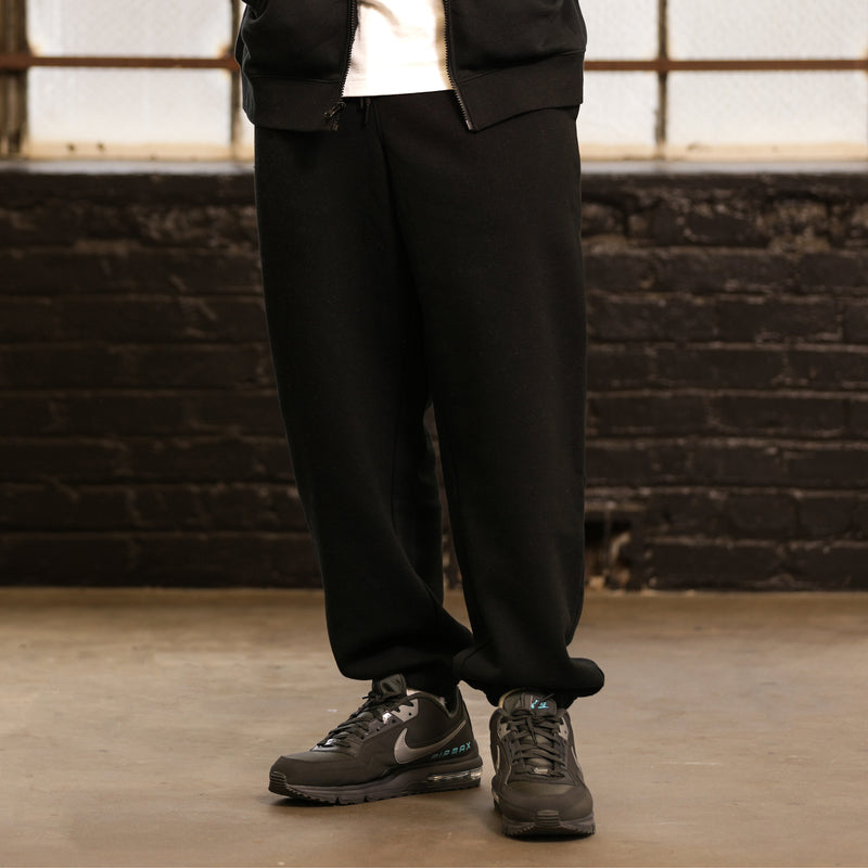 Black men’s fleece sweatpants on model, relaxed fit with cuffed hem and drawstring waist
