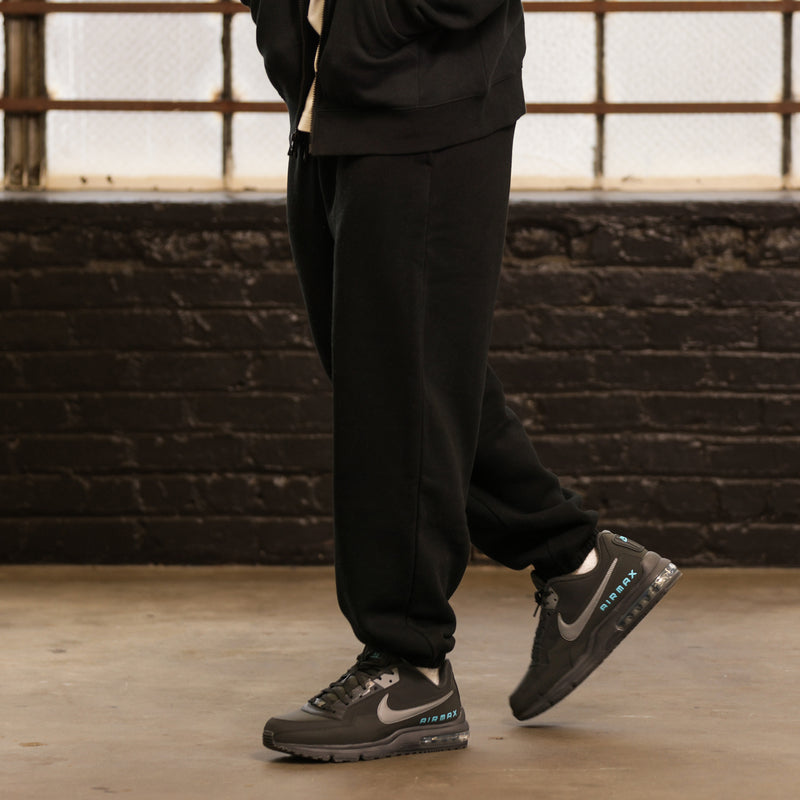 Black men’s fleece sweatpants with tapered leg and cuffed hem; model wears sneakers