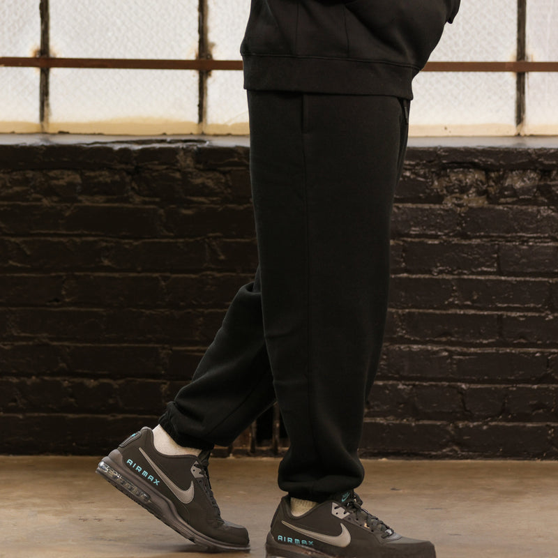 Black men’s fleece sweatpants, relaxed tapered cut with cuffed ankle hem; sneakers visible