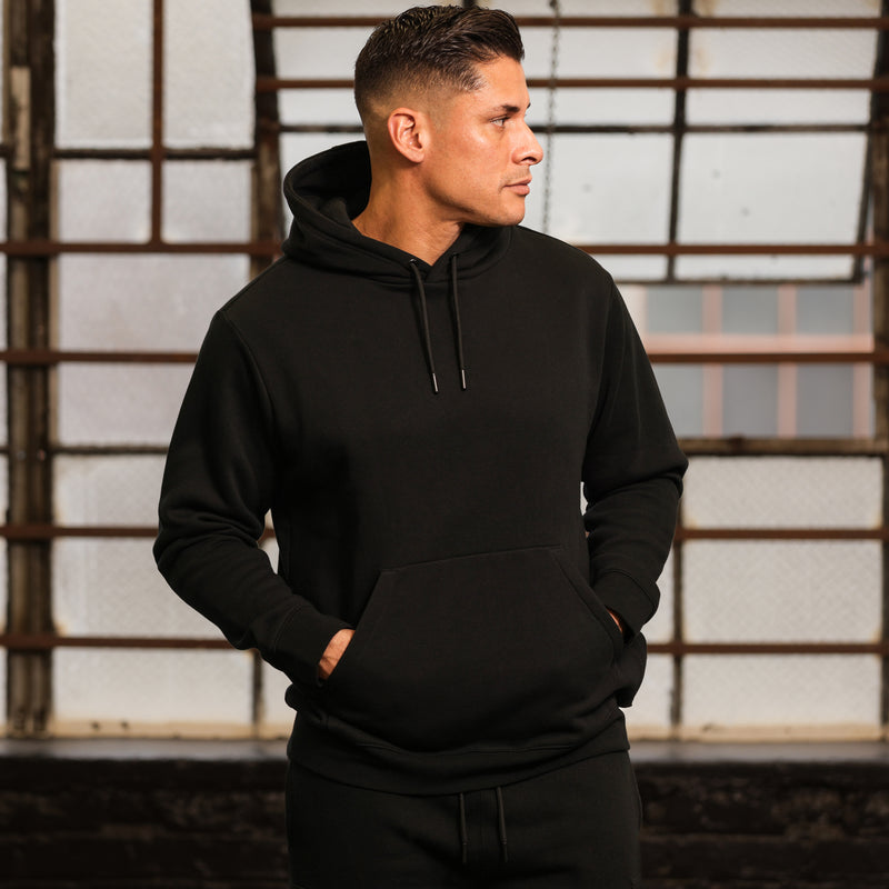 Black fleece pullover hoodie on model, with hood, drawstring, and front kangaroo pocket.
