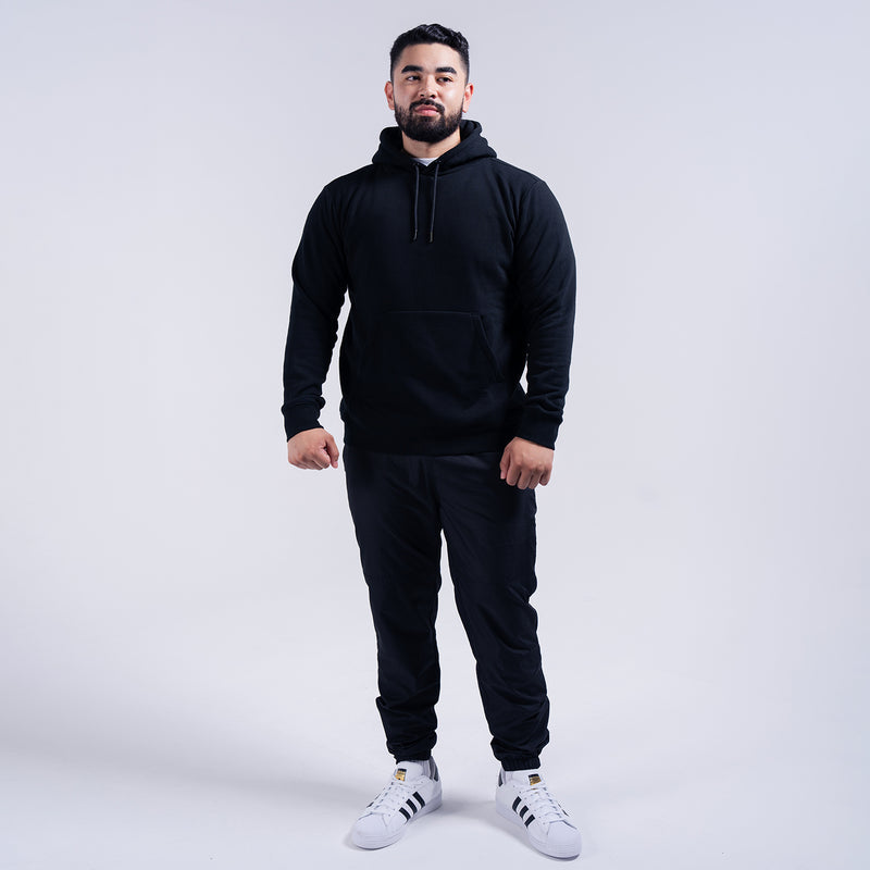 Men's black fleece pullover hoodie with hood and drawstring, paired with dark joggers.
