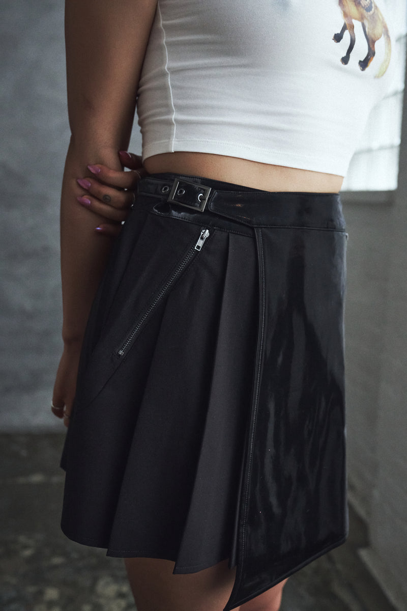 Person wearing a black skirt with zippers and a white top against a gray background