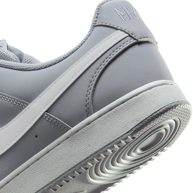 Side close-up of light gray sneaker with white stripe, Nike heel, and grippy sole