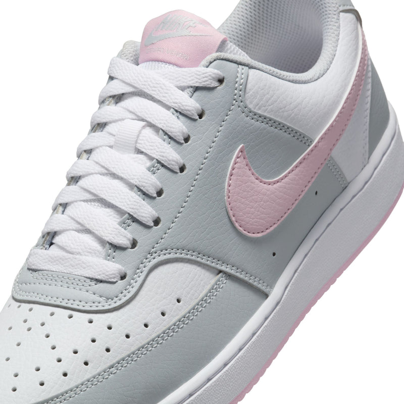 Women’s low-top sneakers close-up: light gray leather, pink swoosh, white laces.