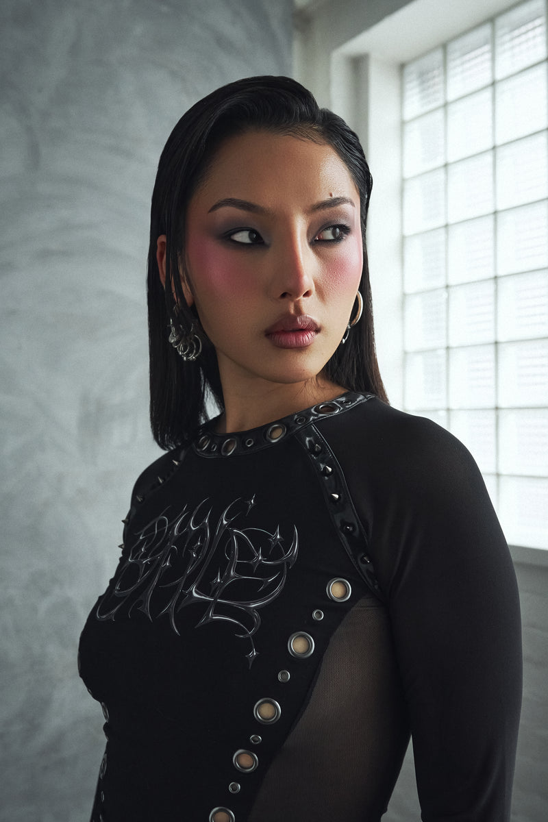 Woman wearing a black outfit with decorative elements in a room with a window.