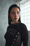 Woman wearing a black outfit with decorative elements in a room with a window.