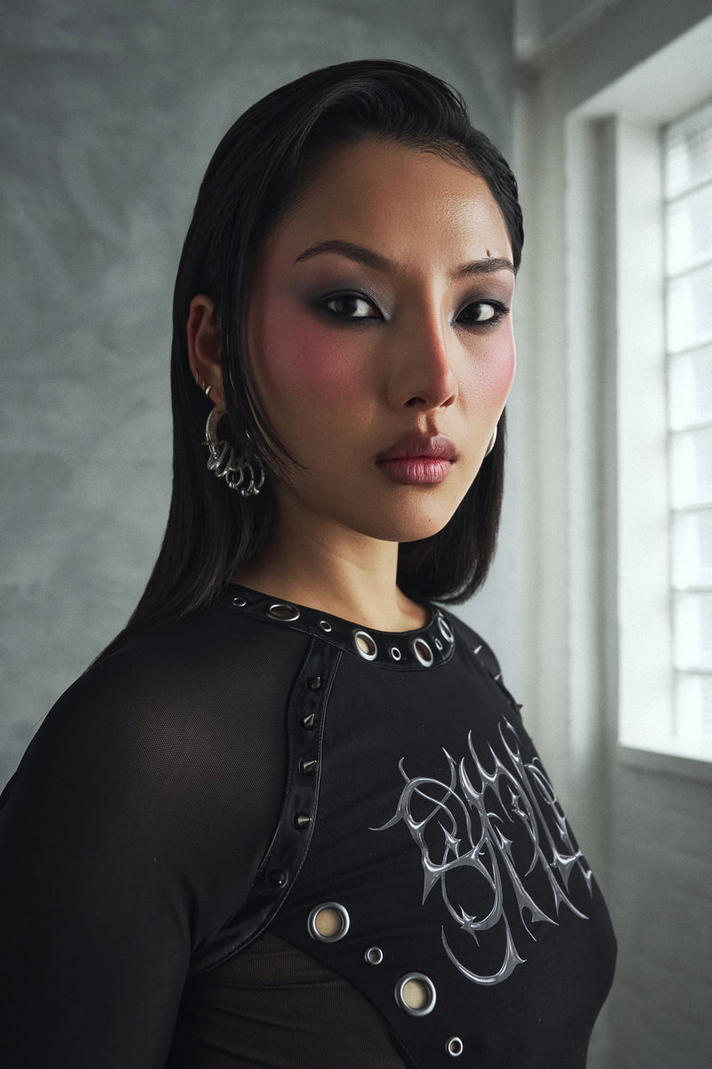 Woman wearing a black outfit with decorative elements in a room with a window.