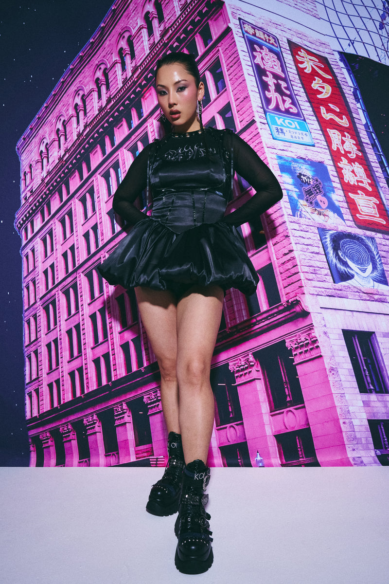 Person wearing a black outfit in front of a pink-lit building with advertisements.
