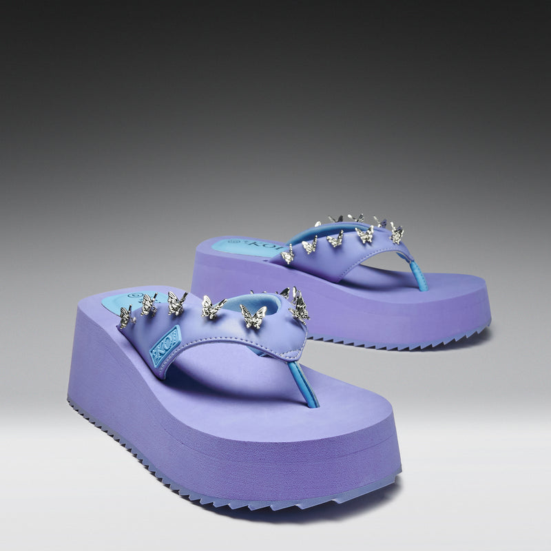 Purple platform sandals with decorative spikes on a gray background