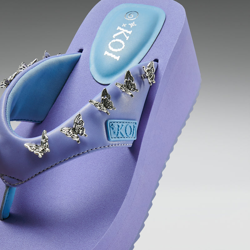 Purple sandal with butterfly decorations and 'Koi' branding on a gray background