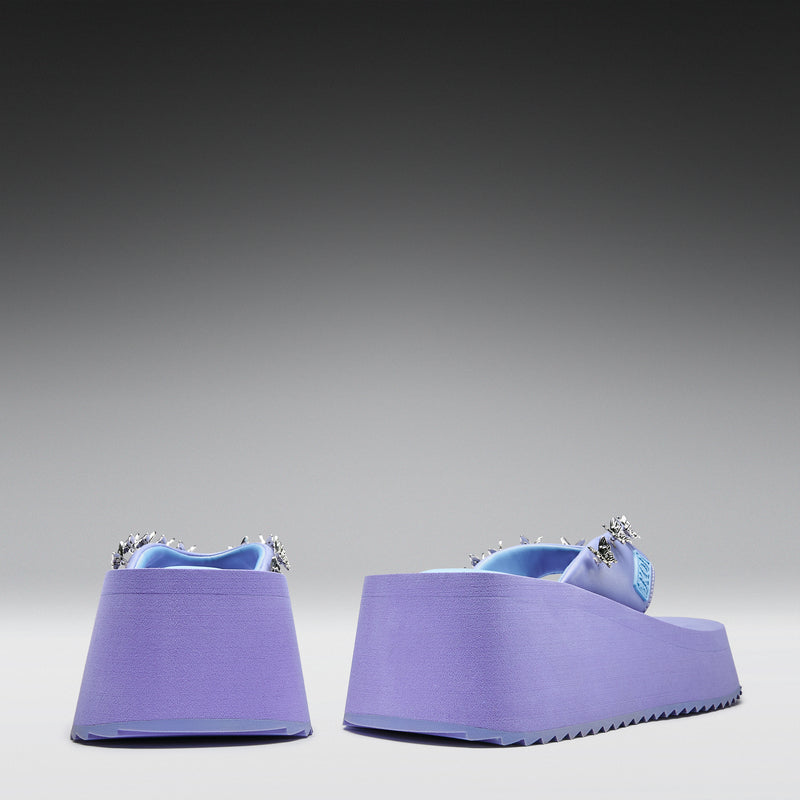 Pair of purple wedge sandals with decorative straps on a gray background