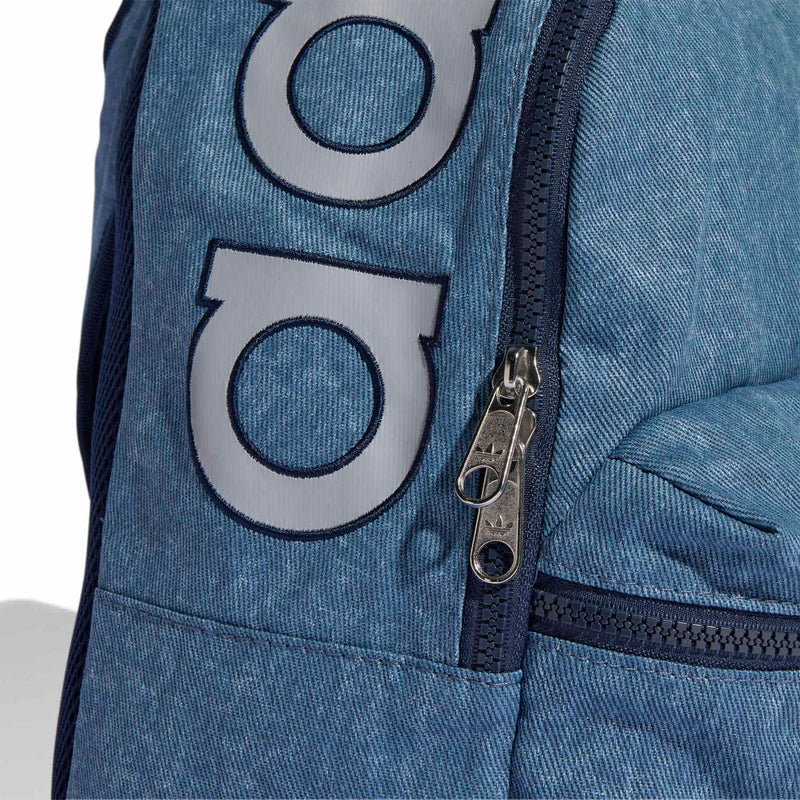 Light denim backpack front with stitched two-tone logo patch and silver zipper pull