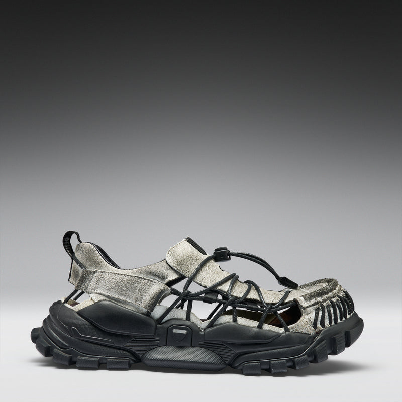 Black and gray sandal with unique sole design on a gradient background