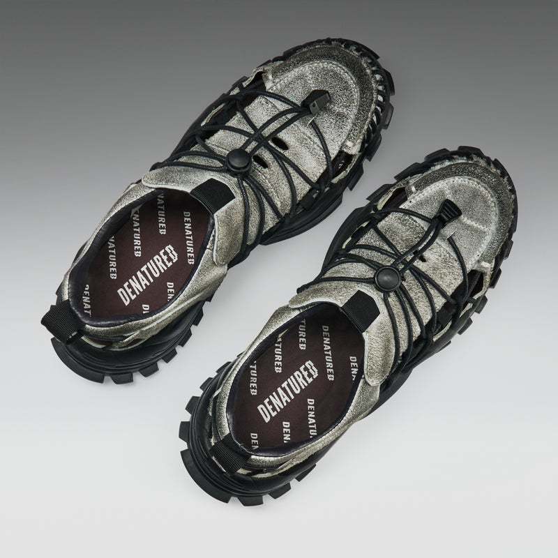 Pair of metallic silver and black shoes with 'Denatured' branding on a gradient background