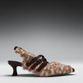 A single women's kitten heel with a brown and beige animal-print faux fur upper, dark brown buckle straps, and a dark brown block heel, shown against a gray gradient studio background.