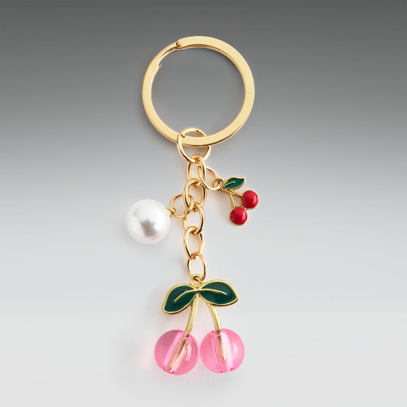 Gold keychain with cherry and pearl charm on a gray background