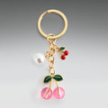Gold keychain with cherry and pearl charm on a gray background