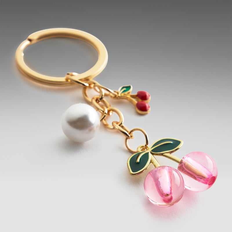 Gold keychain with a pearl, cherry, and pink bead charm on a gray background