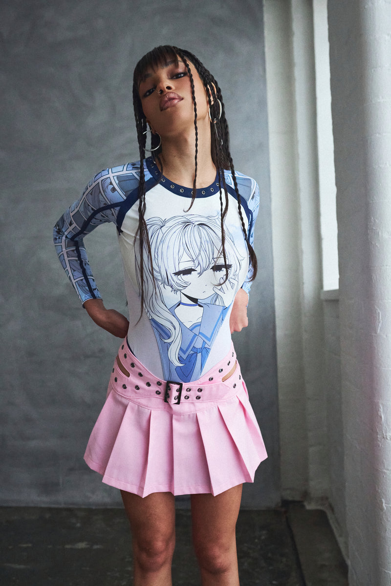 Person wearing a long-sleeve shirt with an anime character design and a pink skirt against a gray wall.