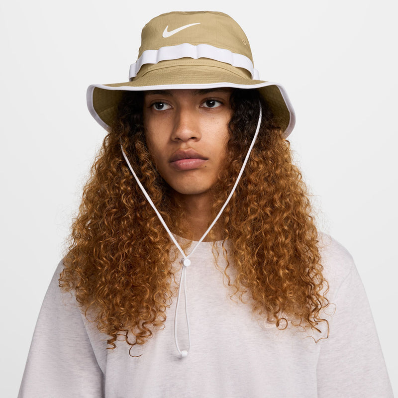 Tan bucket hat with white band, Swoosh logo, and chin cord; model wearing.