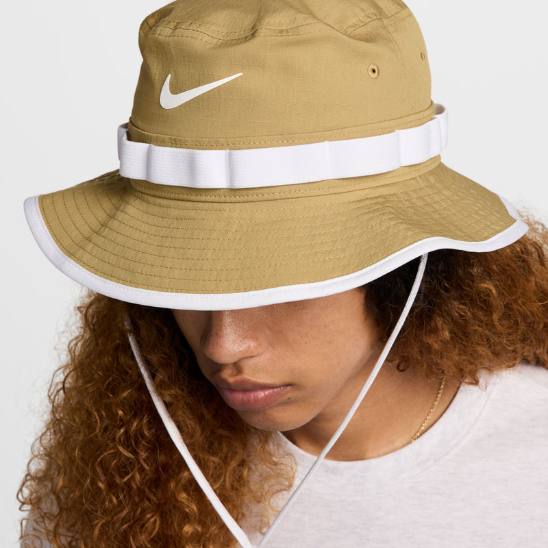 Tan bucket hat close-up with white band, brim trim, and chin cord.