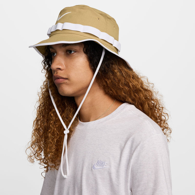 Tan bucket hat with white band, Swoosh logo, and chin cord; side view.