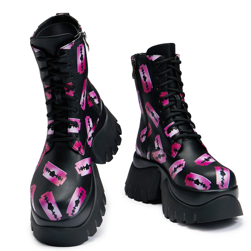 Black platform boots with a pattern of pink razorblade prints, featuring a lace-up front and a chunky sole - front view