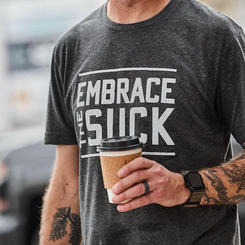 GORUCK charcoal tee with 'Embrace the Suck' text, man holding coffee, outdoor setting