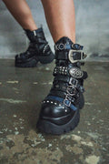 Black platform boots with decorative straps on a concrete floor.