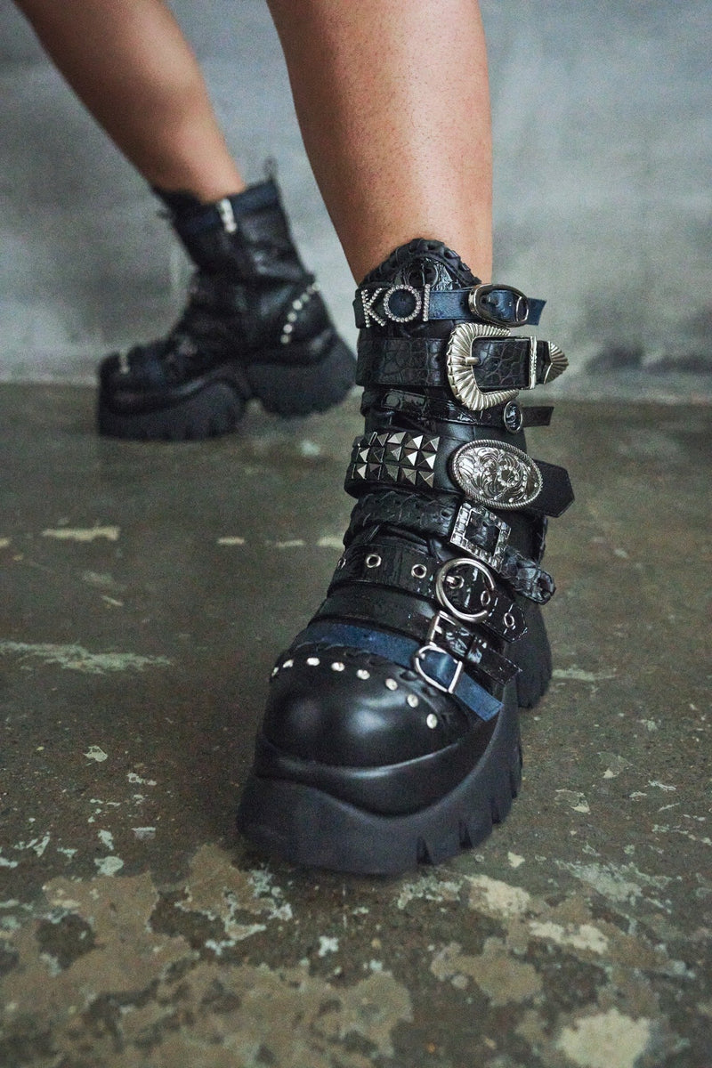 Black platform boots with decorative straps on a concrete floor.