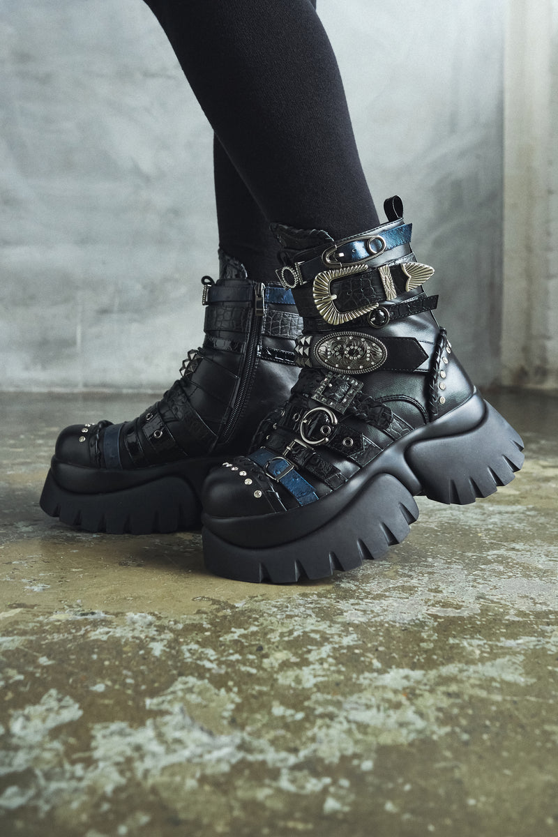 Black platform boots with decorative elements on a textured floor.