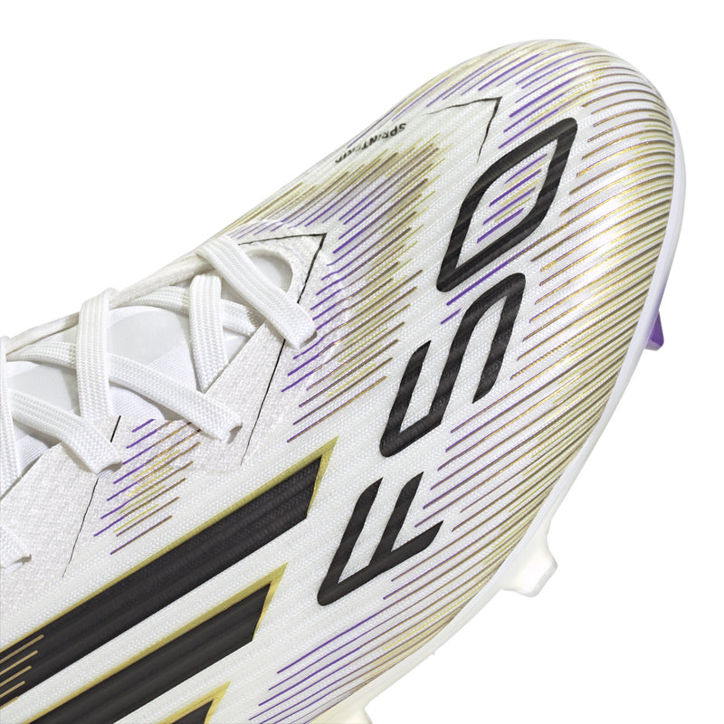 White cleat side view with black streaks, gold accents, and lace-up synthetic upper.