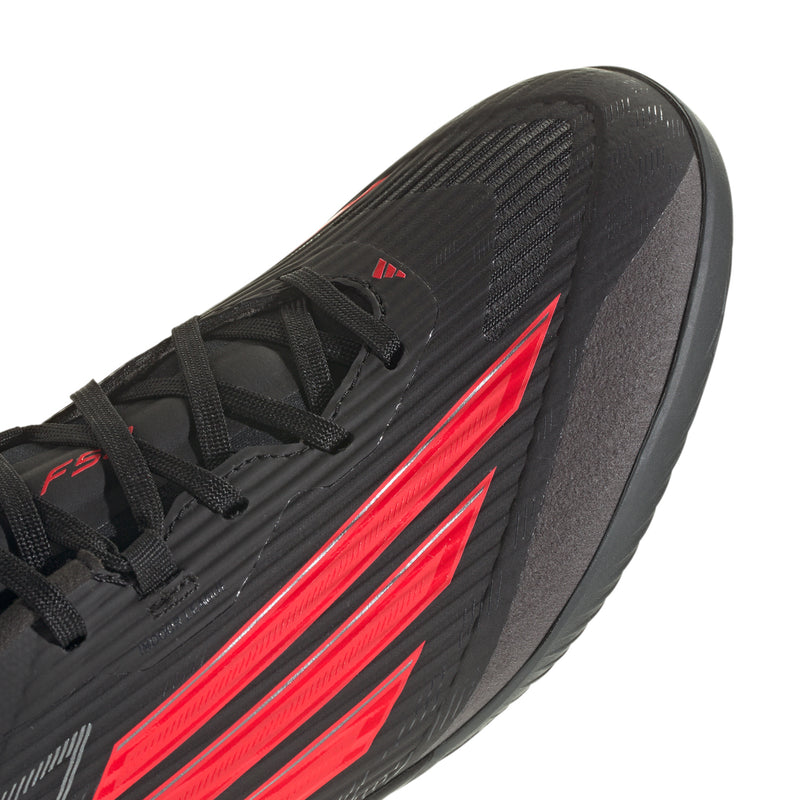 Black soccer cleat upper close-up with red stripes and textured forefoot.